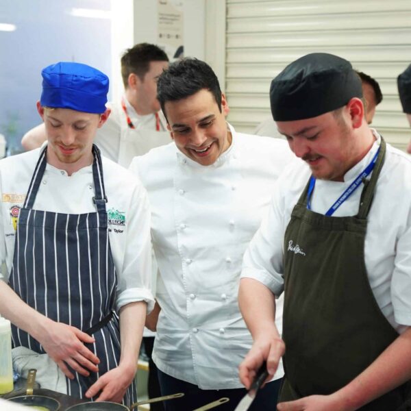Chef Paul Ainsworth watches two student chefs cooking with frying pans.