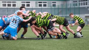 A rugby scrum is taking place between two teams. One team is wearing blue and white stripes and the other is wearing green and black stripes.