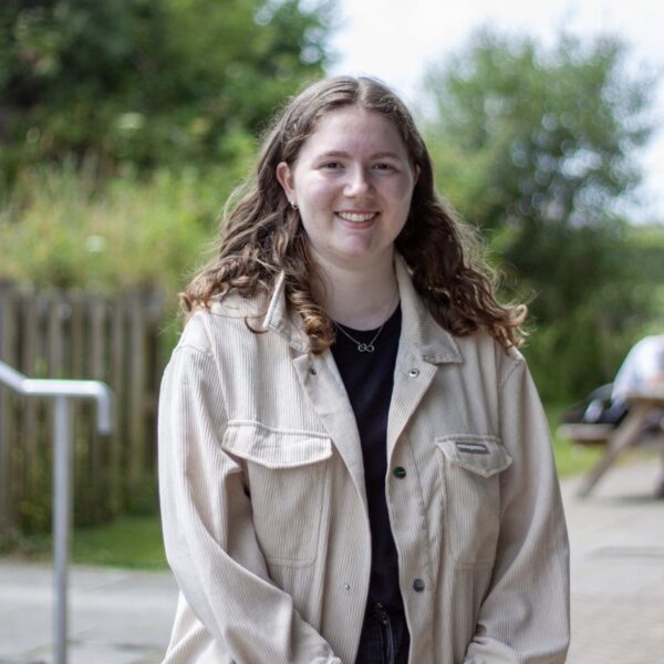 Ellie is stood outside at the college with a picnic bench in the background.
