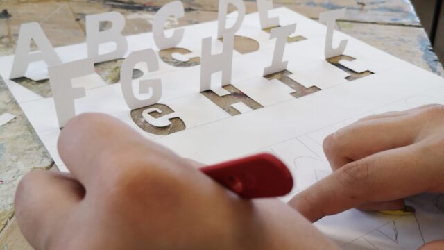 A close up of a hand cutting letters out of paper.
