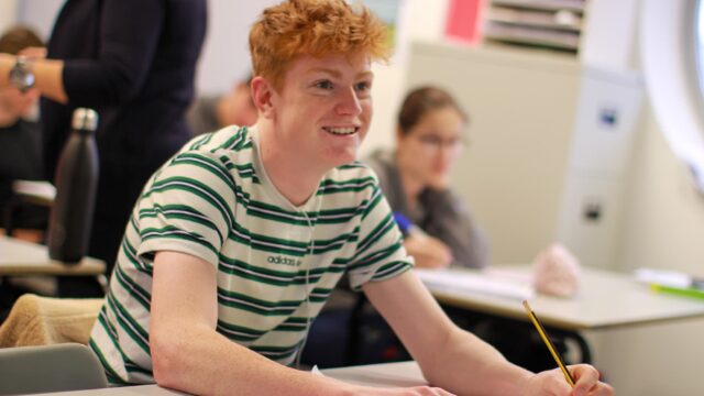A student sat at a classroom table with a pencil in hand.