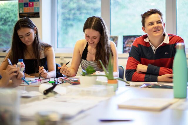 Three students sat at classroom tables with notepads, pens and water bottles.