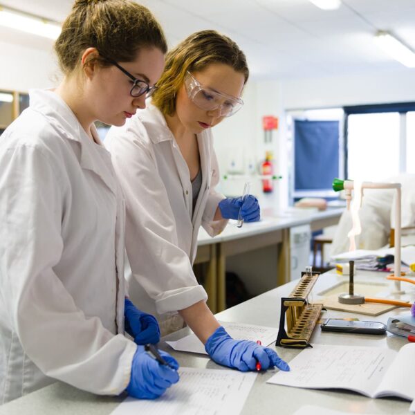 Two students in lab coats are looking at paperwork in a laboratory.