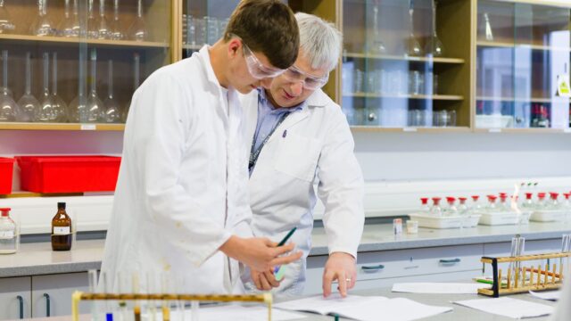A tutor and a student in lab coats looking at paperwork in a laboratory.
