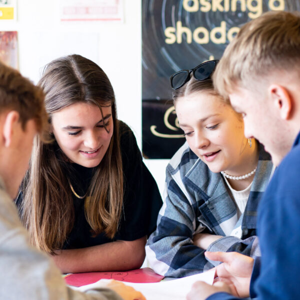 A close up of students looking at something on a table. They are huddled close together.