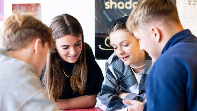 A close up of students looking at something on a table. They are huddled close together.