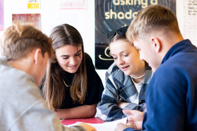 A close up of students looking at something on a table. They are huddled close together.