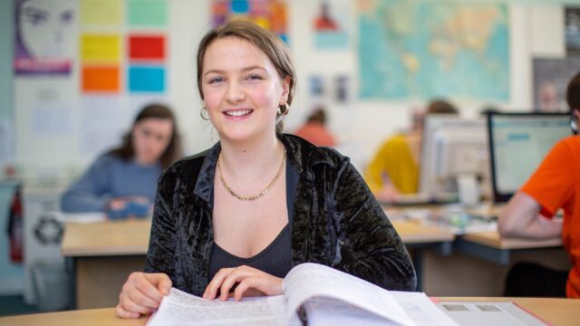 A student smiling at the camera while looking through a folder of notes.