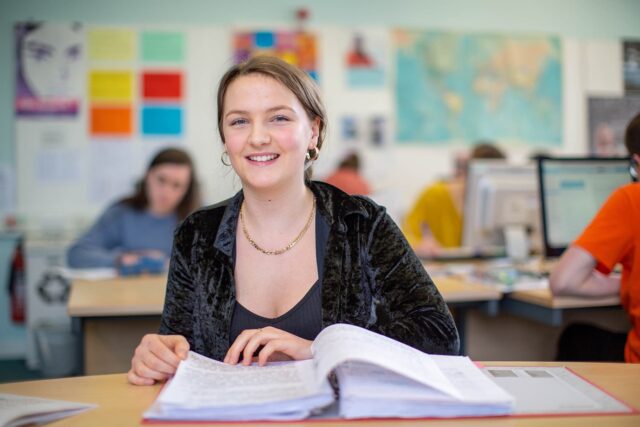 A student smiling at the camera while looking through a folder of notes.