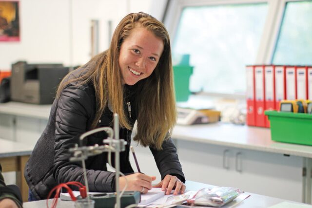 A student in a lab writes in a book with a pen.