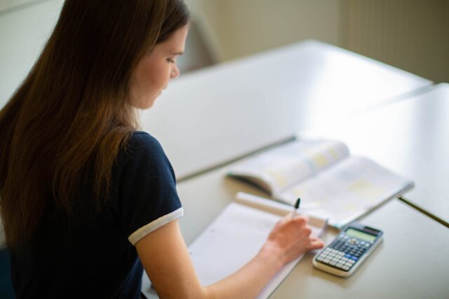 A student sat at a classroom table with notepad and pen and a calculator.