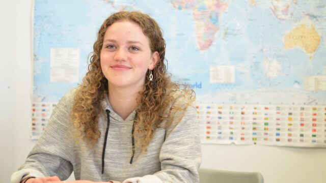 A student sat at a classroom table with a world map behind them.