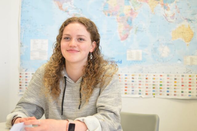 A student sat at a classroom table with a world map behind them.
