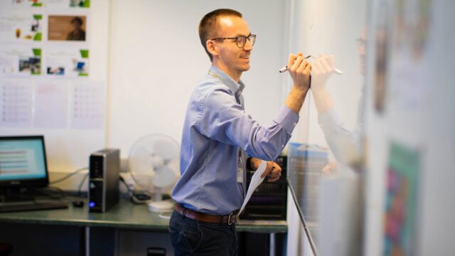 A tutor writing on a whiteboard in a classroom.