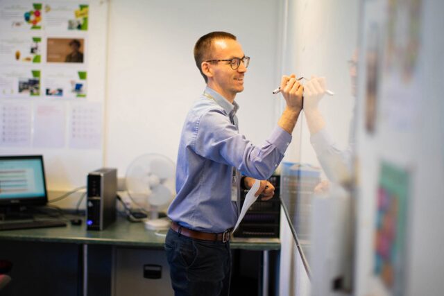 A tutor writing on a whiteboard in a classroom.