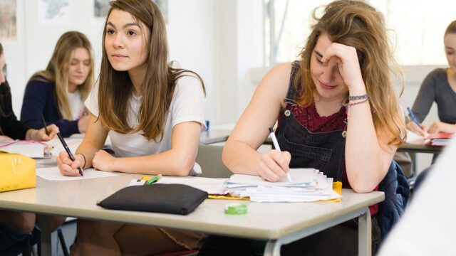Two students sat at a classroom table writing on paper.