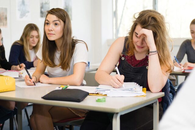 Two students sat at a classroom table writing on paper.
