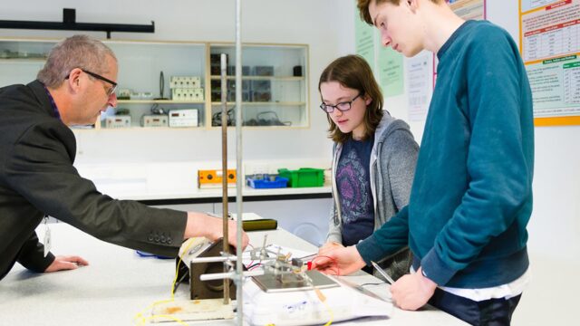 Two students and a tutor in a science classroom looking at equipment together.