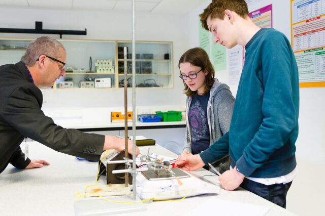 Two students and a tutor in a science classroom looking at equipment together.