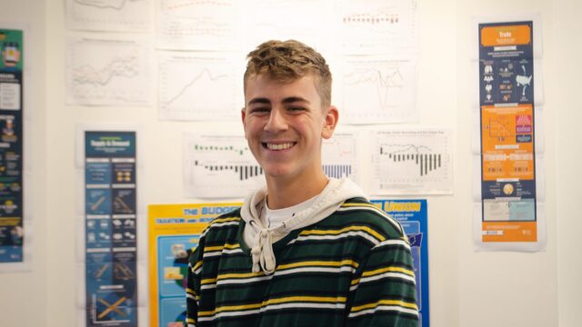 A student smiling. In the background there is a wall covered in posters.