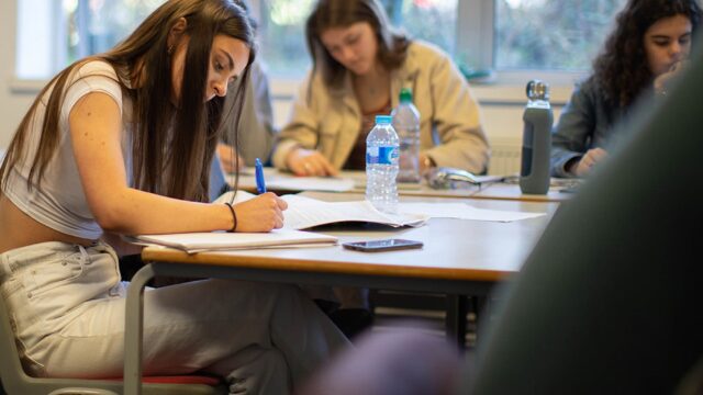 Students sitting at classroom tables writing in notebooks.