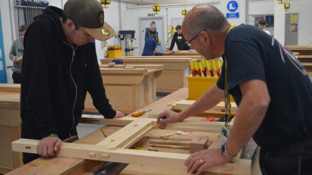A tutor and a student look at a piece of woodwork together.