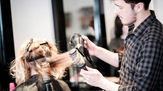 A male hairdresser blowdrying a client's hair.