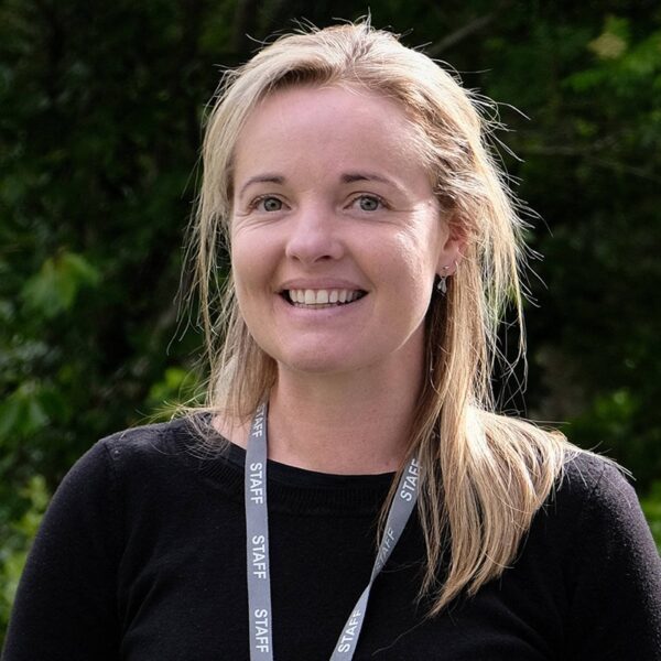 A photo of Angela smiling. She is wearing a black top and her staff lanyard.