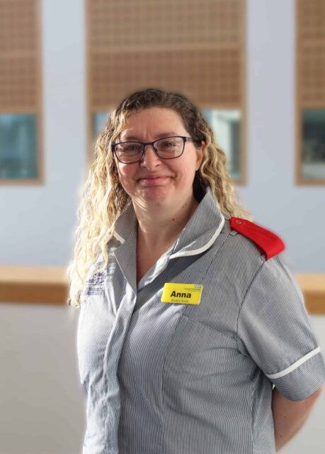 Anna is wearing a nurses uniform and stands with her hands behind her back.