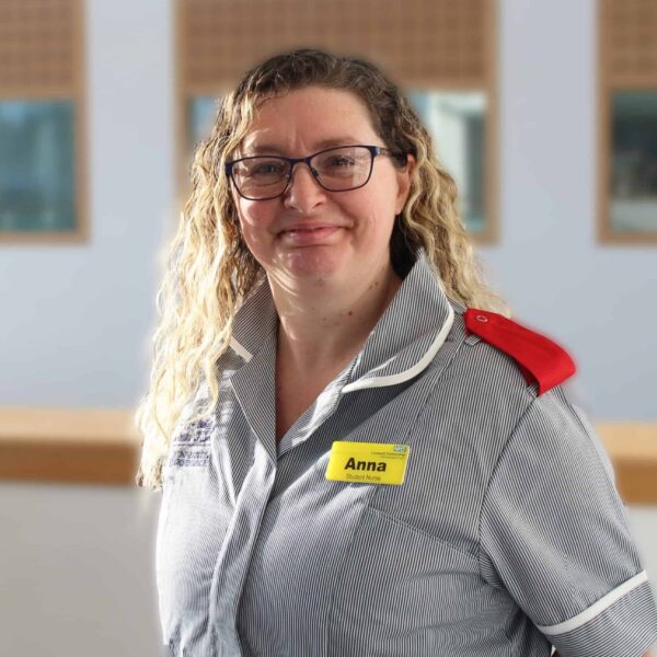 Anna is wearing a nurses uniform and stands with her hands behind her back.