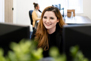 An apprentice with red hair looks at a computer in an office.