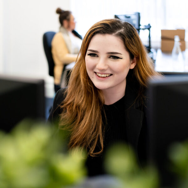An apprentice with red hair looks at a computer in an office.