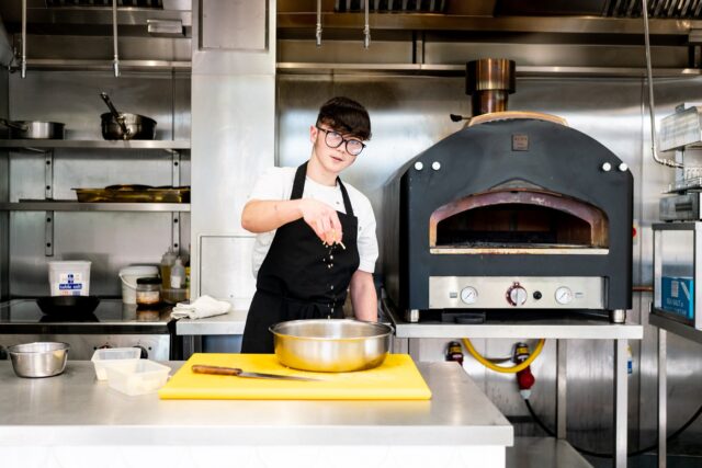 A chef sprinkles cheese in a bowl in a kitchen.