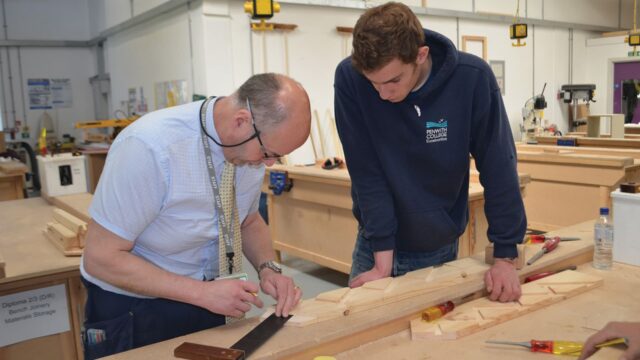 A tutor and student are looking at wood during a bench joinery class.