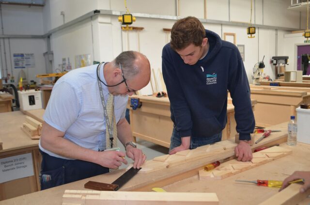A tutor and student are looking at wood during a bench joinery class.