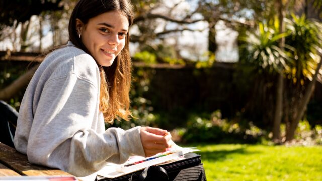 A student sitting outside painting with watercolours.