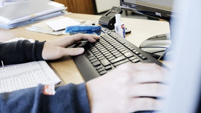 Close up of hands resting on a keyboard on an office desk.