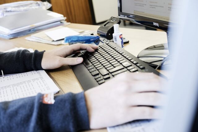Close up of hands resting on a keyboard on an office desk.