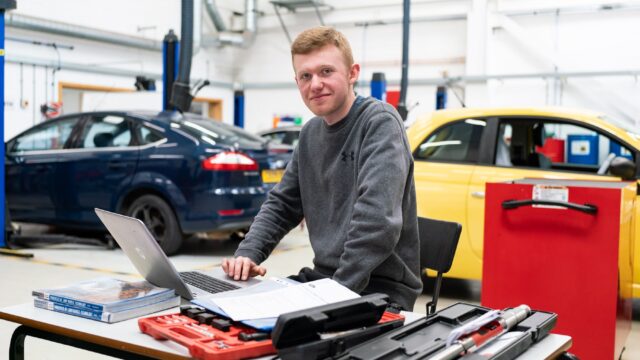A student sits in a garage with a laptop.
