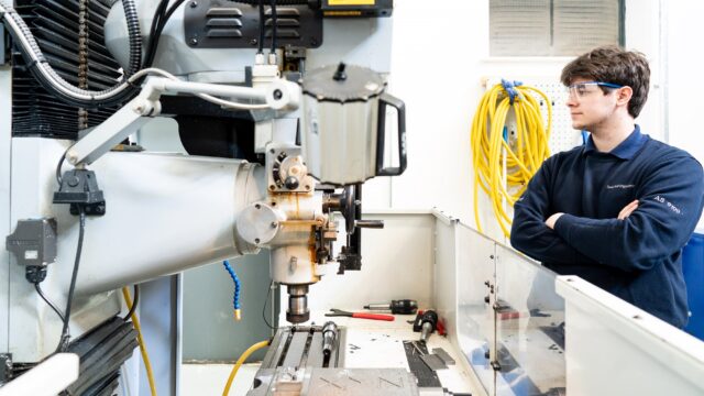 An engineering student with his arms folded looking at engineering equipment.