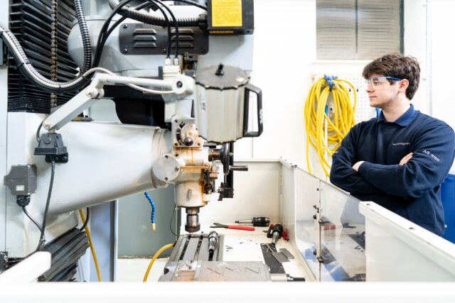 An engineering student with his arms folded looking at engineering equipment.