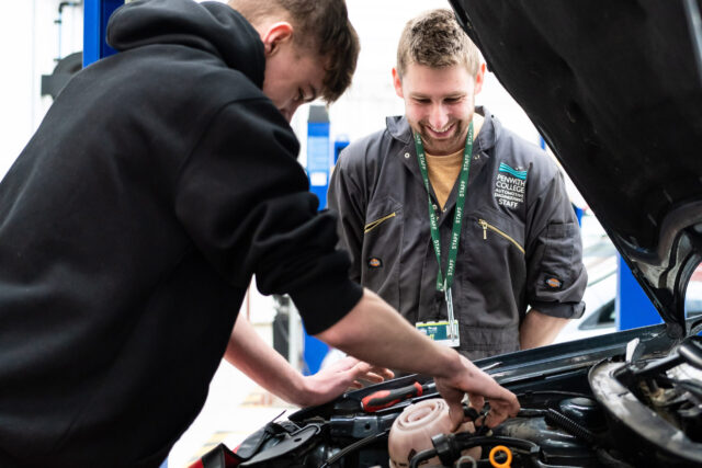 A tutor watches as a student looks under the bonnet of a car.