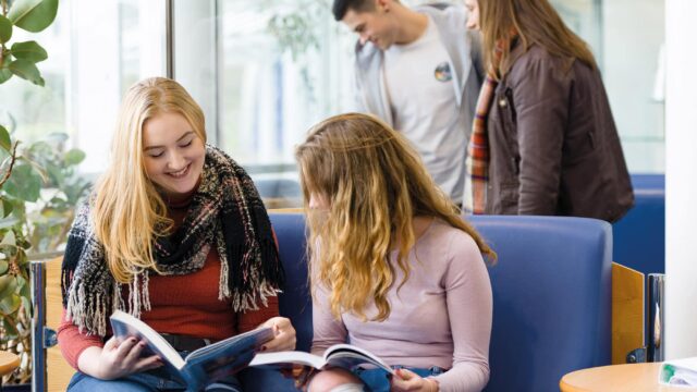 Two students sit on a sofa and look at books together.