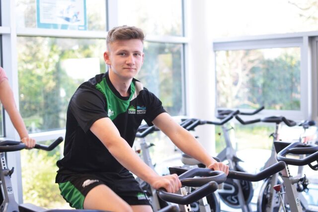 A student on an exercise bike in a college gym.