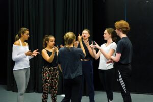 A group of drama students in a circle performing hand gestures.