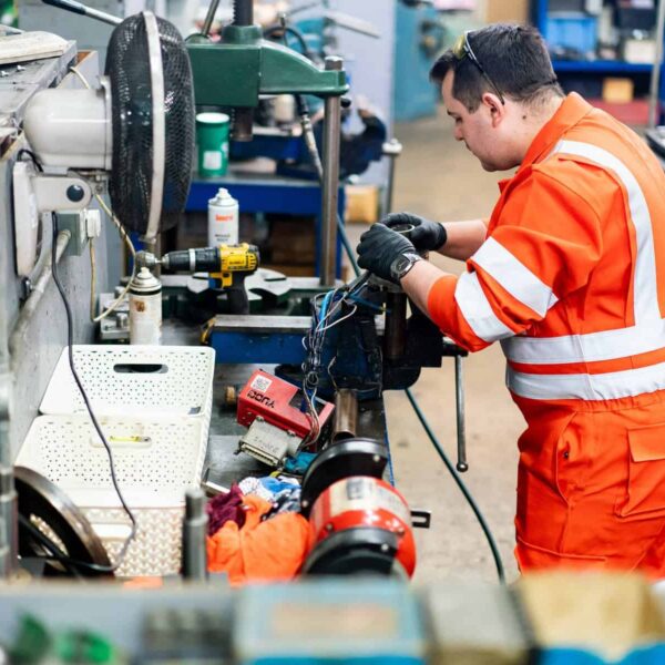 An apprentice in orange overalls works on a piece of machinery.