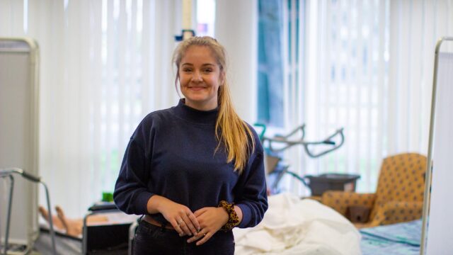 A student stands in front of a hospital bed and smiles.