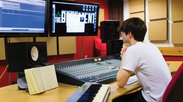 A student sitting at computers and music technology equipment.