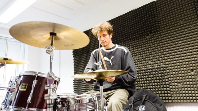 A student playing the drums in a music studio at the College.