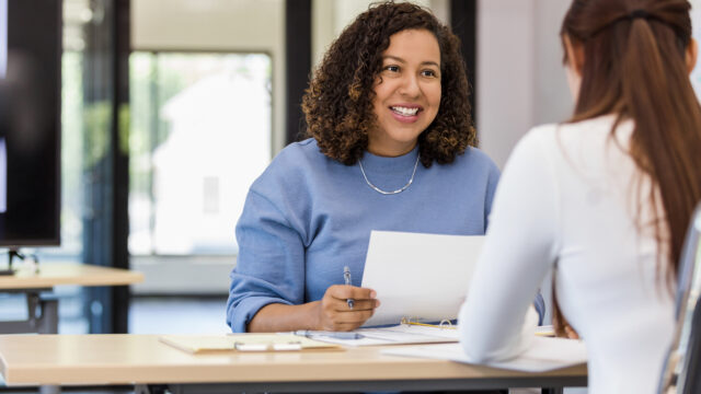 The office manager holds onto a resume while speaking with the new intern they are considering.